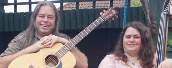 Photograph of David Rozzell wearing a OOO-18 acoustic guitar, stood next to Clare Rozzell leaning on a double bass.